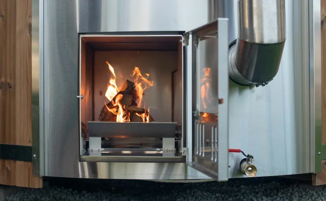 Stainless steel wood-burning stove with the door open and a fire inside