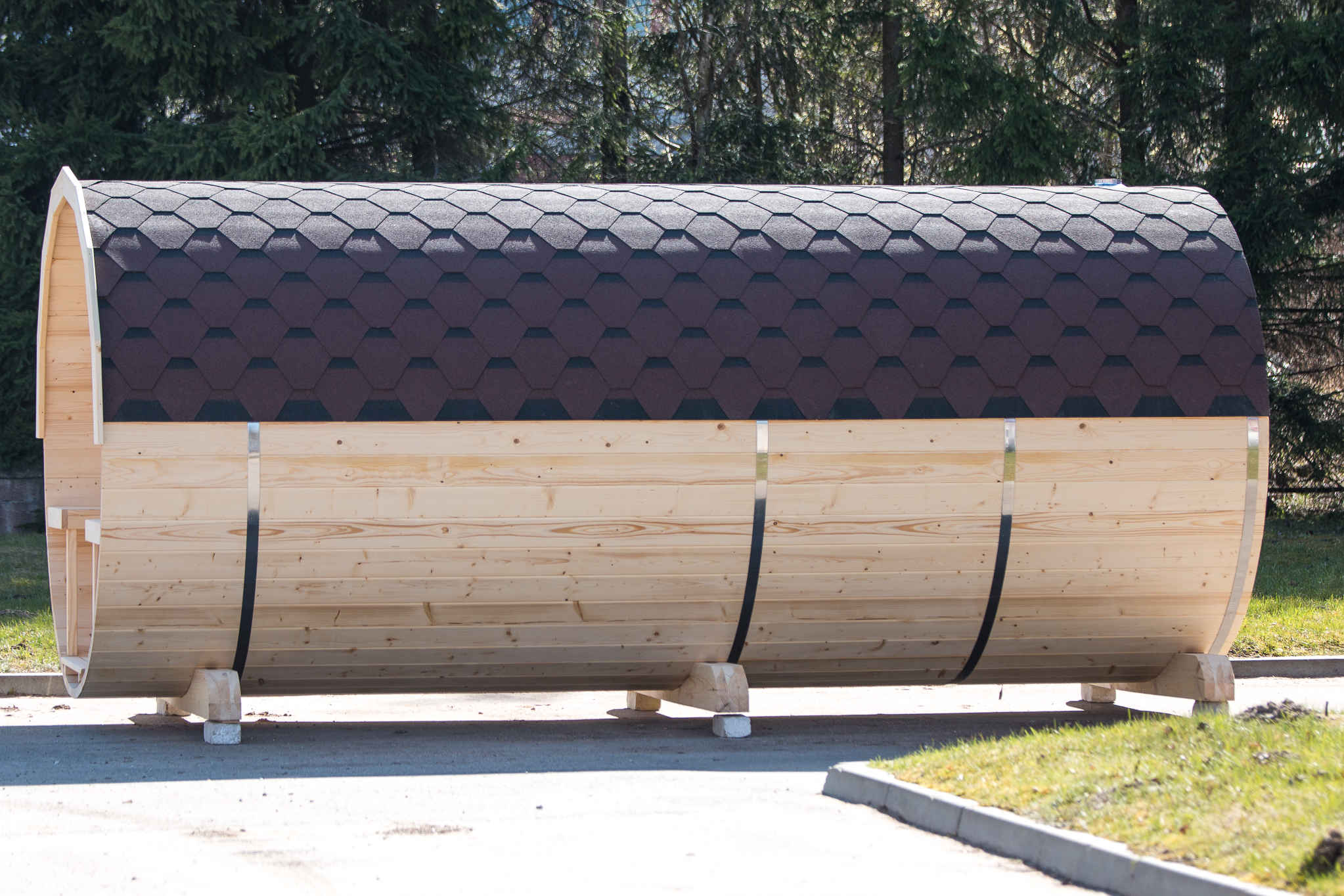 A Royal Tubs barrel sauna with a shingle roof standing on a base