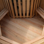 Interior of a wooden sauna with benches along walls and a hexagonal wooden floor pattern.