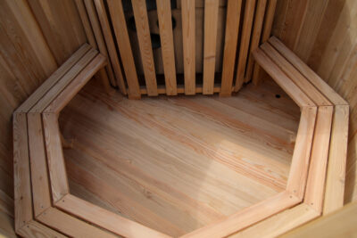 Interior of a wooden sauna with benches along walls and a hexagonal wooden floor pattern.