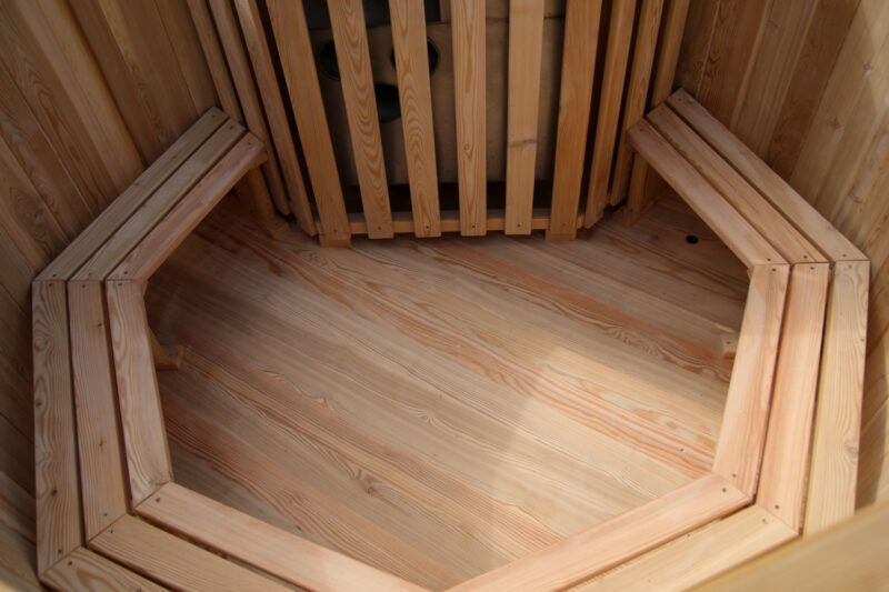 Interior of a wooden sauna with benches along walls and a hexagonal wooden floor pattern.