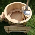 A wooden octagonal hot tub with built-in benches, steps, and a metal stove pipe, on grass.