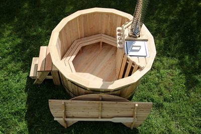 A wooden octagonal hot tub with built-in benches, steps, and a metal stove pipe, on grass.