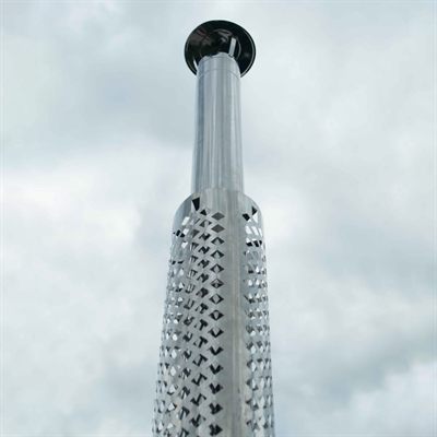 Tall metallic chimney with perforated outer pattern against cloudy sky.