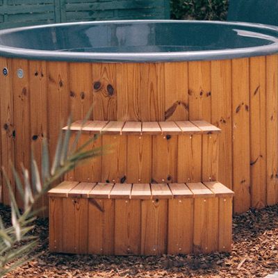 Outdoor wooden hot tub with two-step wooden stairs and mulch ground.