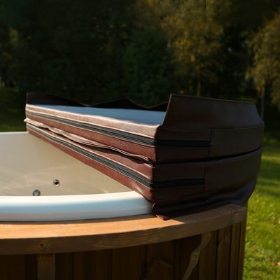Brown padded cushion stack with zippers on the edge of a white hot tub outdoors.