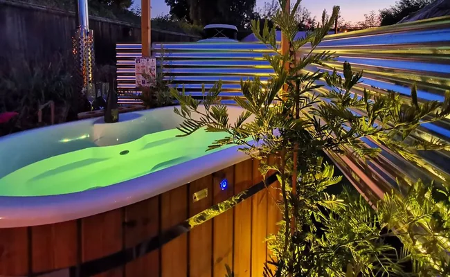 Hot tub lit with green LED lighting in a garden at dusk